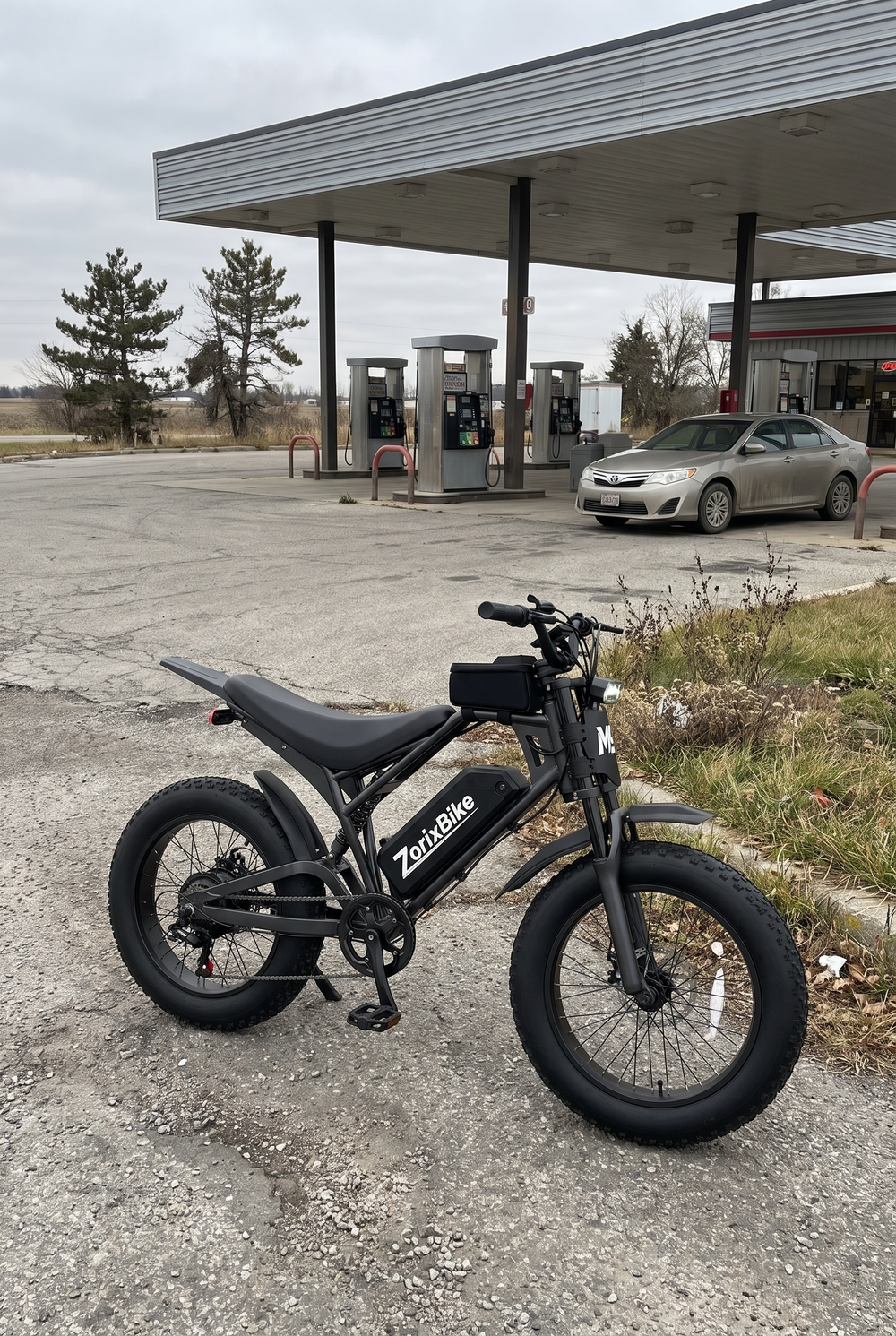 Real photos of ZorixBike M9 Electric bike parked in front of a gas station with a car in the background.